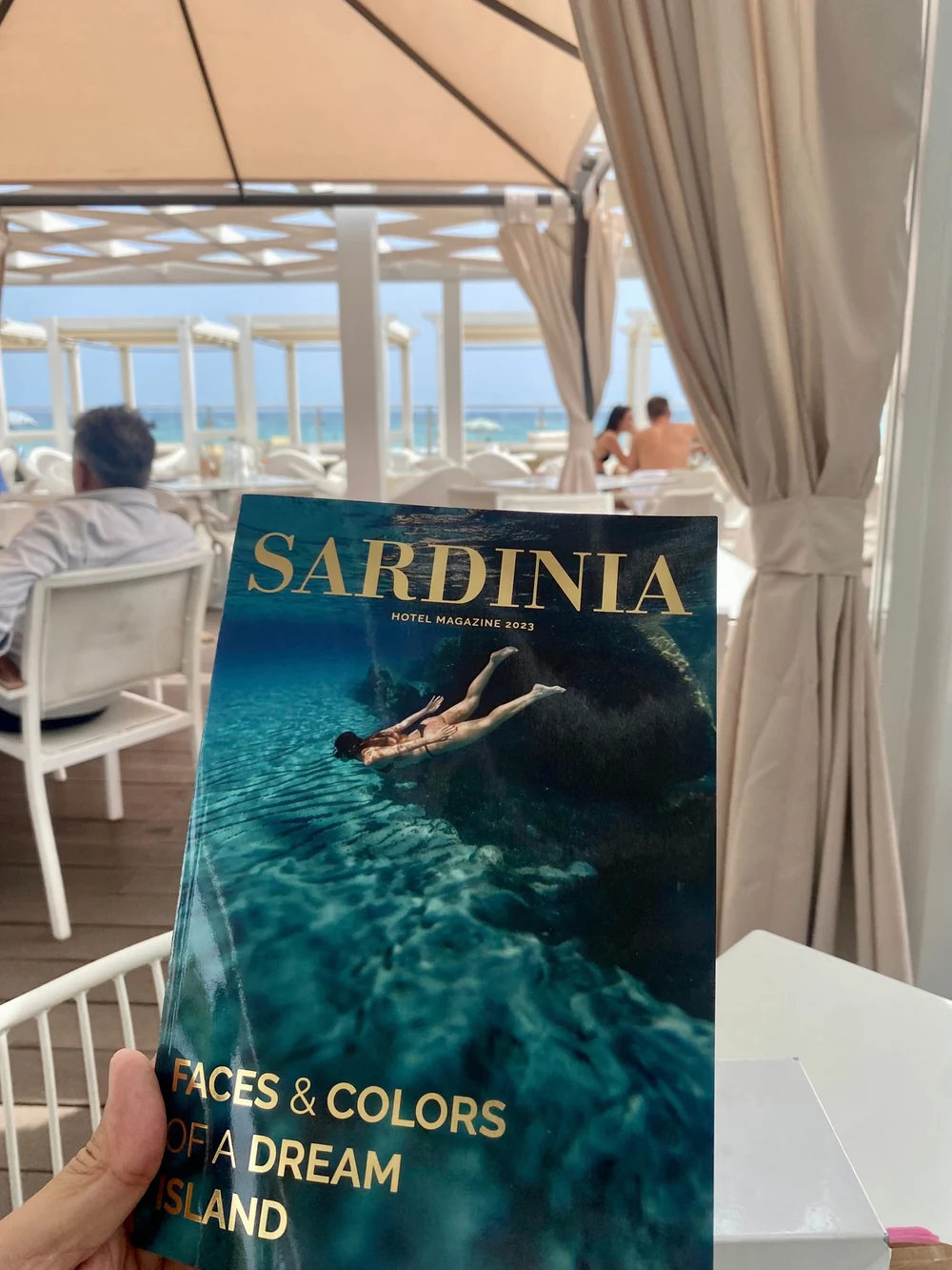 Una copia di Sardinia Magazine tenuta in mano in uno spazio affacciato sul mare; fotografia d’archivio dal Mediakit 2027